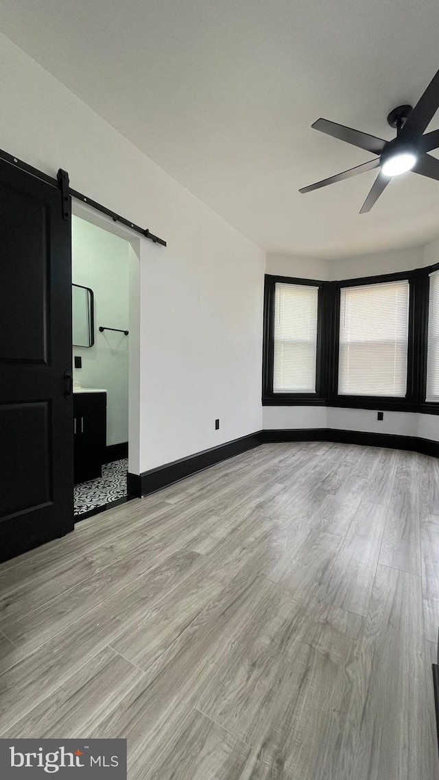 unfurnished room with light wood-type flooring, a barn door, and ceiling fan