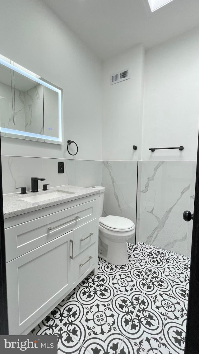 bathroom featuring tile patterned floors, vanity, toilet, and tile walls