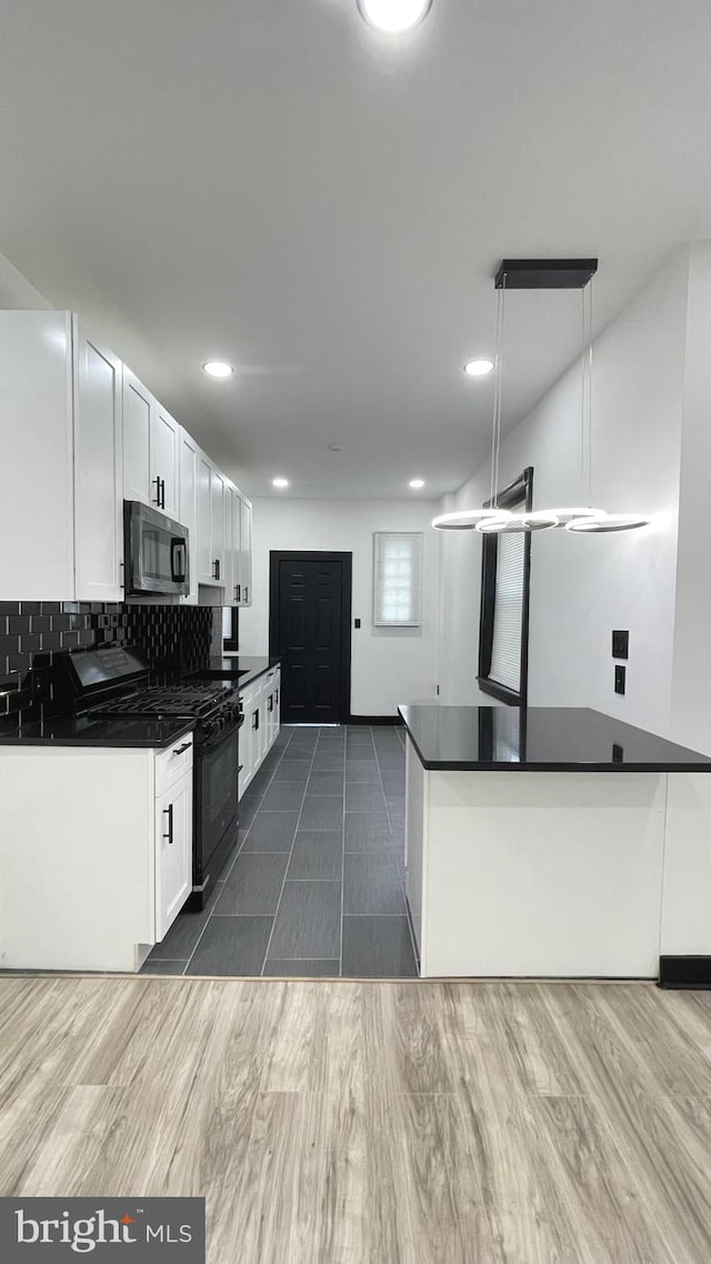 kitchen featuring pendant lighting, black gas range, kitchen peninsula, decorative backsplash, and white cabinetry