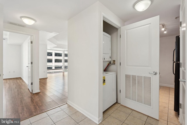 hall featuring stacked washer and clothes dryer and light tile patterned flooring