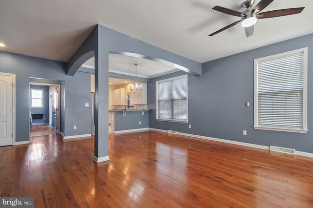 unfurnished living room featuring ceiling fan with notable chandelier and dark wood-type flooring