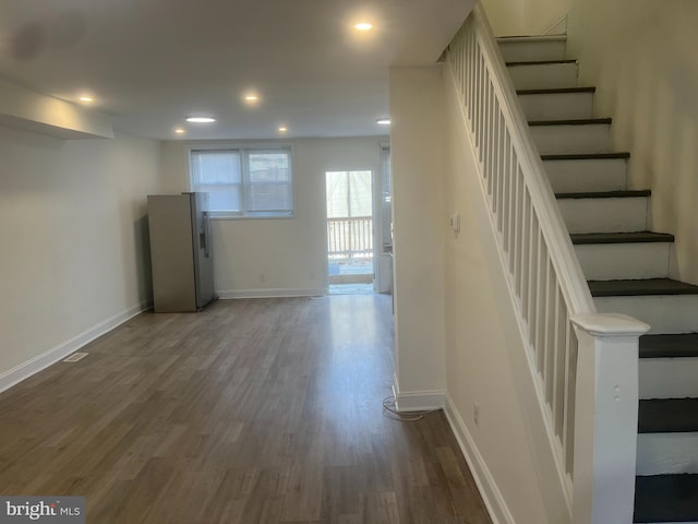 basement featuring dark hardwood / wood-style floors and stainless steel refrigerator with ice dispenser