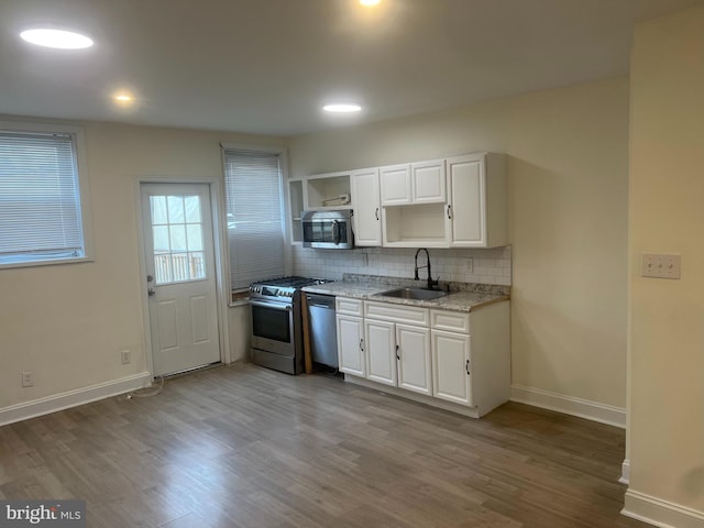 kitchen featuring white cabinets, sink, light wood-type flooring, light stone countertops, and appliances with stainless steel finishes