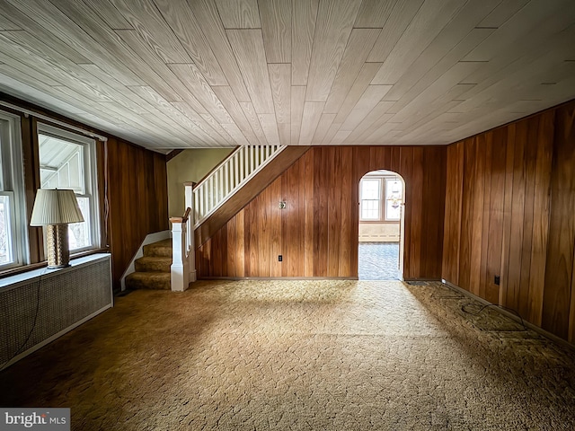 unfurnished living room featuring carpet floors, plenty of natural light, wood walls, and wood ceiling