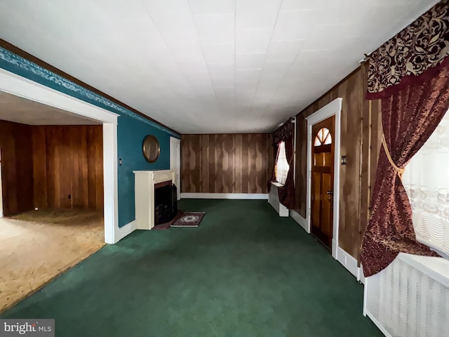 unfurnished living room with wood walls, crown molding, and dark colored carpet