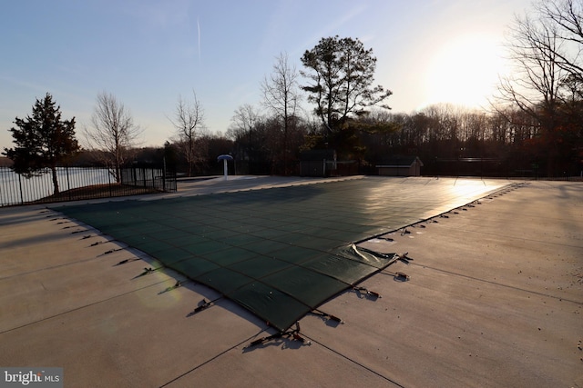 pool at dusk with a patio area and fence