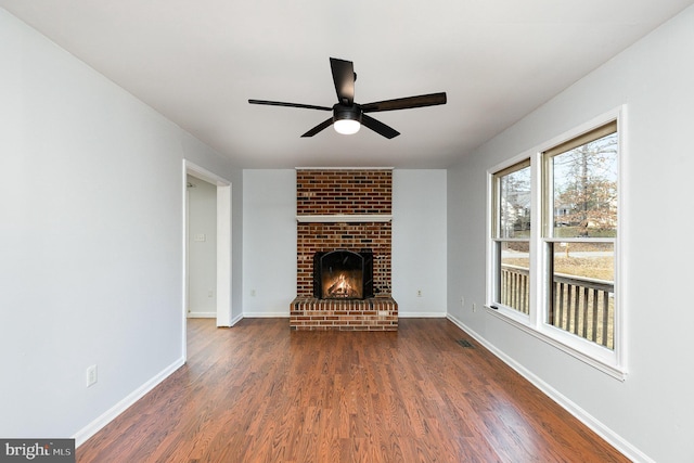 unfurnished living room featuring a ceiling fan, a brick fireplace, wood finished floors, and baseboards