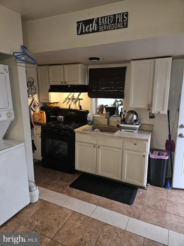 kitchen with black range with gas cooktop, sink, light tile patterned floors, stacked washer and dryer, and white cabinetry