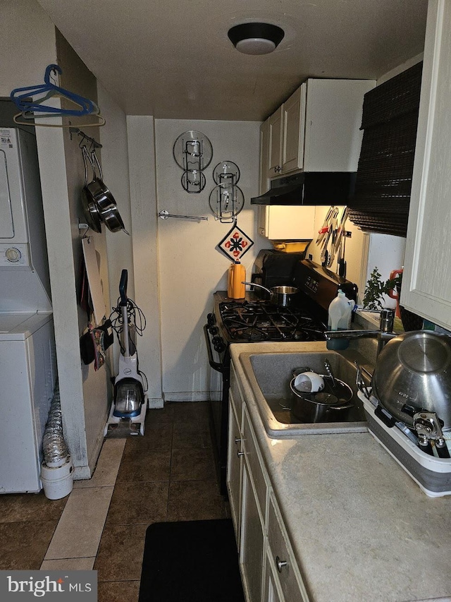 kitchen featuring black range with gas stovetop, white cabinetry, dark tile patterned floors, and stacked washer and clothes dryer