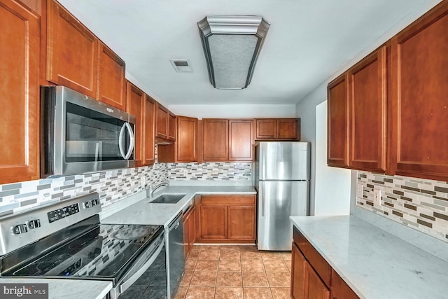 kitchen with light stone countertops, sink, tasteful backsplash, light tile patterned floors, and appliances with stainless steel finishes