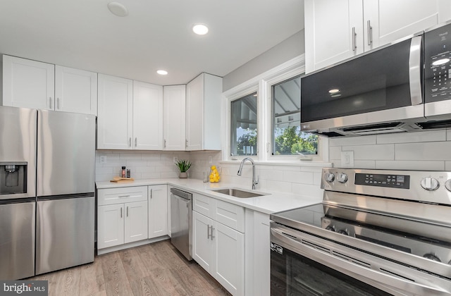 kitchen featuring decorative backsplash, appliances with stainless steel finishes, light wood-type flooring, sink, and white cabinetry