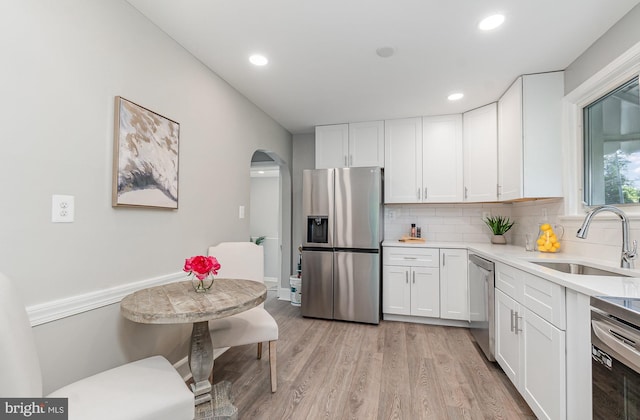 kitchen featuring light wood-type flooring, tasteful backsplash, stainless steel appliances, sink, and white cabinetry