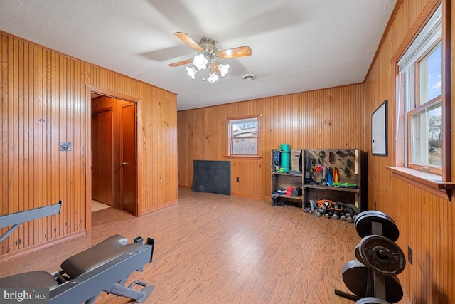 exercise area with ceiling fan, light wood-type flooring, and wooden walls