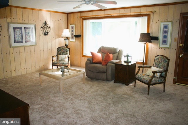 sitting room with ceiling fan, crown molding, carpet floors, and wood walls