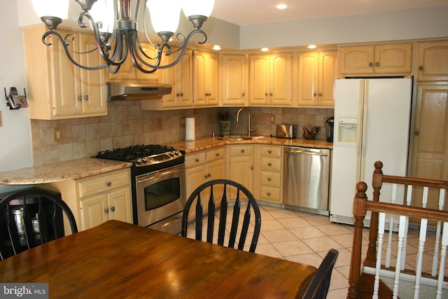 kitchen featuring light stone countertops, stainless steel appliances, sink, light tile patterned floors, and an inviting chandelier