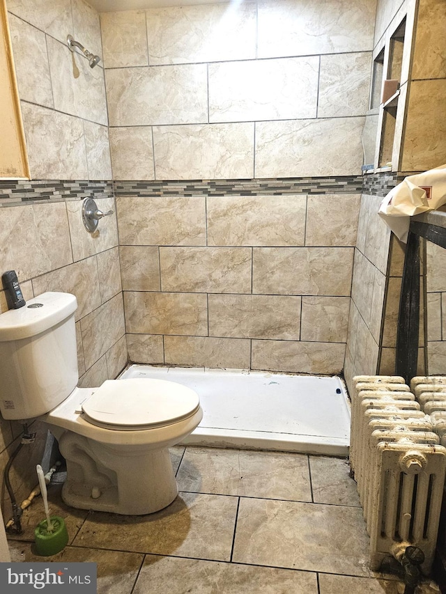 bathroom featuring a tile shower, radiator heating unit, tile walls, and toilet