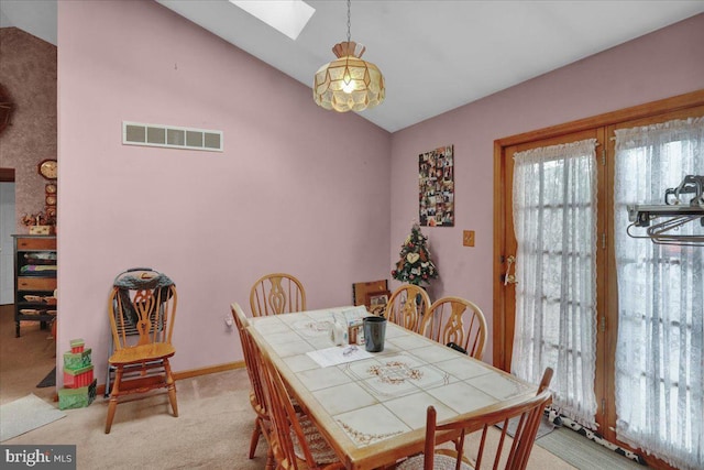 carpeted dining space with lofted ceiling with skylight