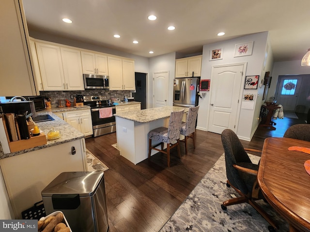 kitchen with light stone countertops, a center island, dark wood-type flooring, and appliances with stainless steel finishes