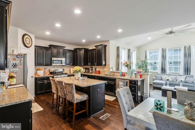 kitchen with decorative backsplash, appliances with stainless steel finishes, a kitchen breakfast bar, dark wood-type flooring, and a center island