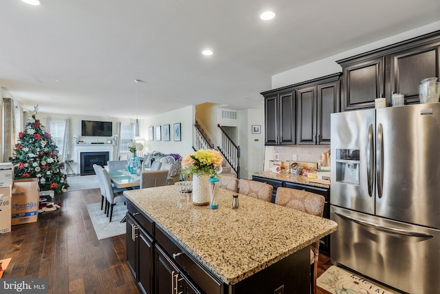 kitchen with stainless steel refrigerator with ice dispenser, backsplash, light stone counters, dark wood-type flooring, and a center island