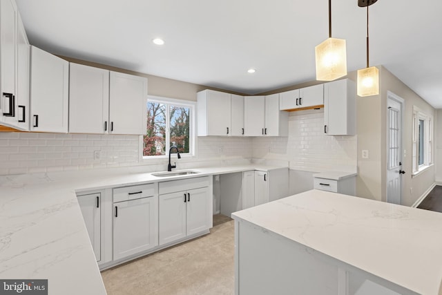 kitchen featuring white cabinets, light stone counters, hanging light fixtures, and sink