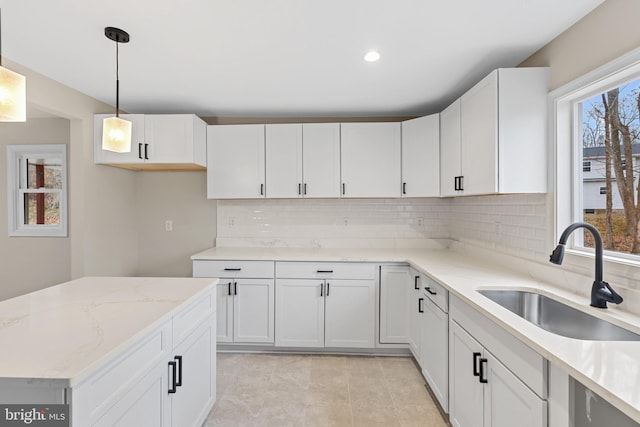 kitchen featuring backsplash, white cabinets, sink, light stone countertops, and decorative light fixtures