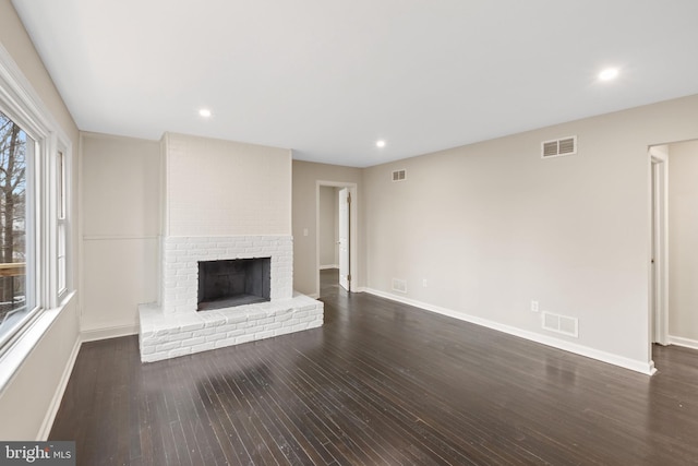 unfurnished living room featuring a brick fireplace and dark wood-type flooring