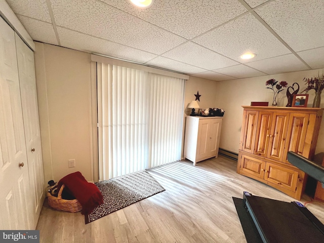 interior space with a drop ceiling, light hardwood / wood-style floors, and a baseboard heating unit