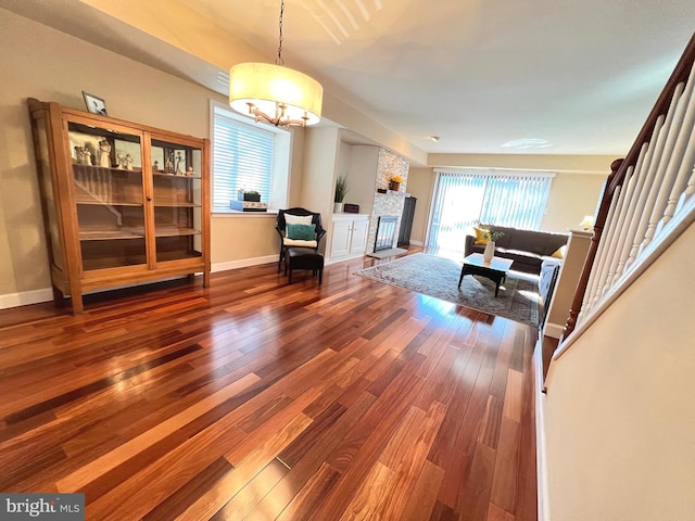 living room with dark hardwood / wood-style flooring, a fireplace, a wealth of natural light, and an inviting chandelier