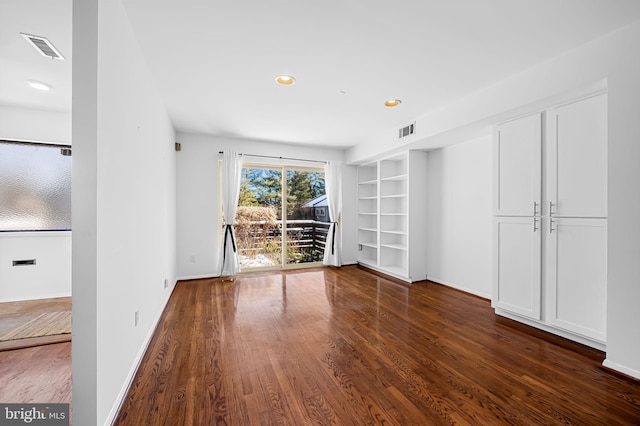 empty room with built in shelves and dark hardwood / wood-style floors