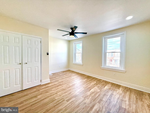 unfurnished bedroom featuring multiple windows, ceiling fan, light hardwood / wood-style flooring, and a textured ceiling