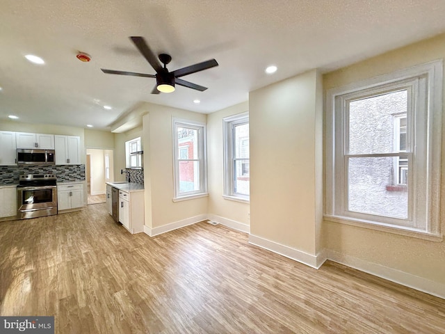 kitchen with light wood-type flooring, tasteful backsplash, stainless steel appliances, ceiling fan, and white cabinets