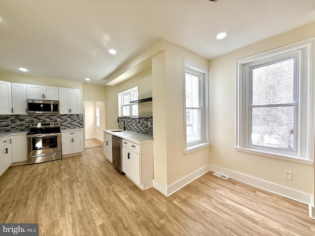 kitchen featuring white cabinets, sink, tasteful backsplash, light hardwood / wood-style floors, and stainless steel appliances