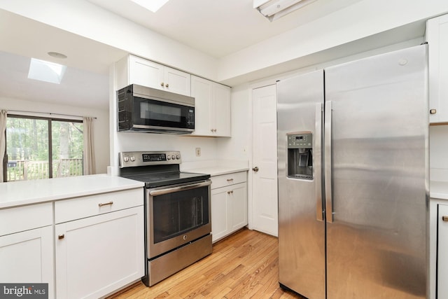 kitchen featuring a skylight, light hardwood / wood-style flooring, white cabinets, and appliances with stainless steel finishes