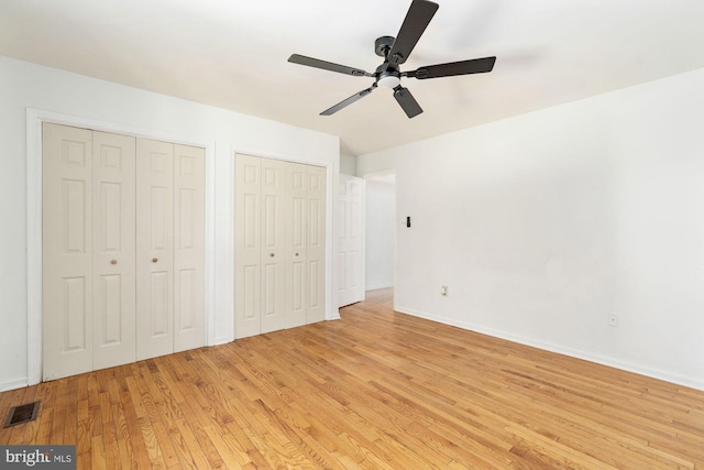 unfurnished bedroom with ceiling fan, light wood-type flooring, and two closets