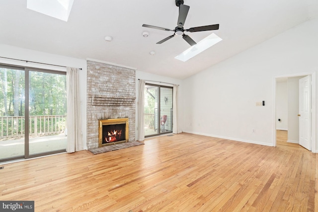 unfurnished living room with a fireplace, ceiling fan, vaulted ceiling with skylight, and light hardwood / wood-style flooring