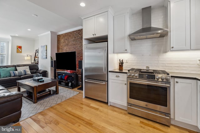 kitchen with white cabinets, crown molding, light hardwood / wood-style flooring, wall chimney exhaust hood, and appliances with stainless steel finishes