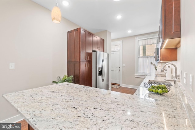 kitchen with light stone countertops, sink, hanging light fixtures, stainless steel refrigerator with ice dispenser, and kitchen peninsula