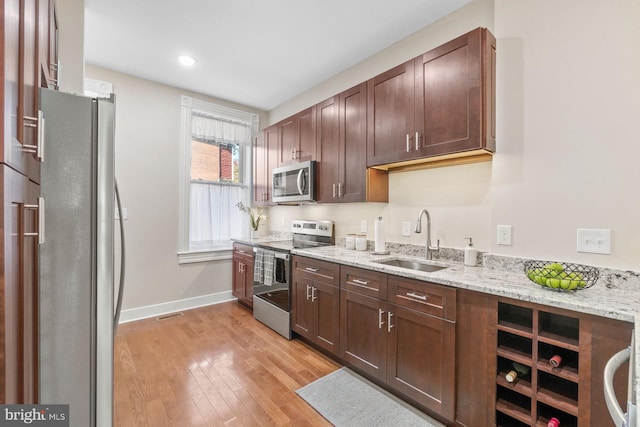 kitchen with light stone countertops, appliances with stainless steel finishes, light hardwood / wood-style flooring, and sink