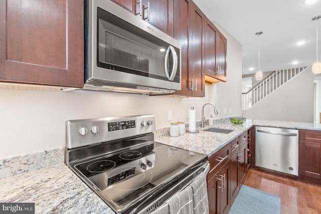 kitchen with kitchen peninsula, light stone counters, stainless steel appliances, sink, and hanging light fixtures