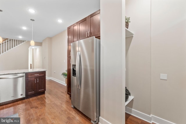 kitchen featuring dark brown cabinetry, appliances with stainless steel finishes, decorative light fixtures, light stone counters, and wood-type flooring