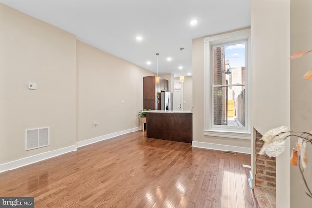 interior space with pendant lighting, stainless steel fridge, and hardwood / wood-style flooring