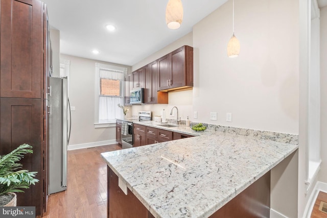 kitchen featuring sink, hanging light fixtures, light stone countertops, kitchen peninsula, and stainless steel appliances