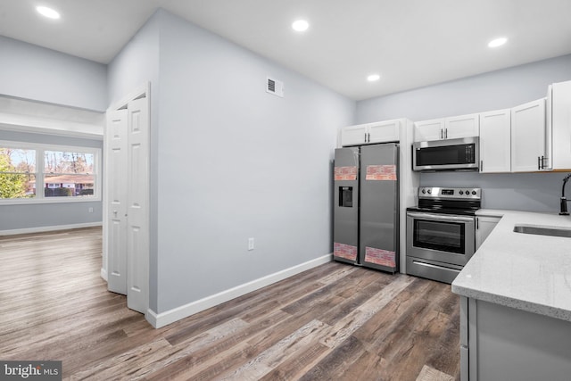 kitchen with light stone counters, stainless steel appliances, sink, white cabinets, and dark hardwood / wood-style floors