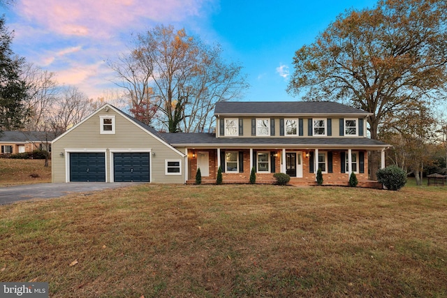 colonial-style house featuring a porch, a yard, and a garage