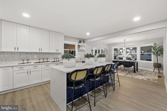 kitchen with a kitchen bar, light stone counters, decorative light fixtures, a center island, and white cabinetry