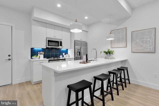 kitchen featuring kitchen peninsula, decorative light fixtures, stainless steel appliances, and white cabinetry