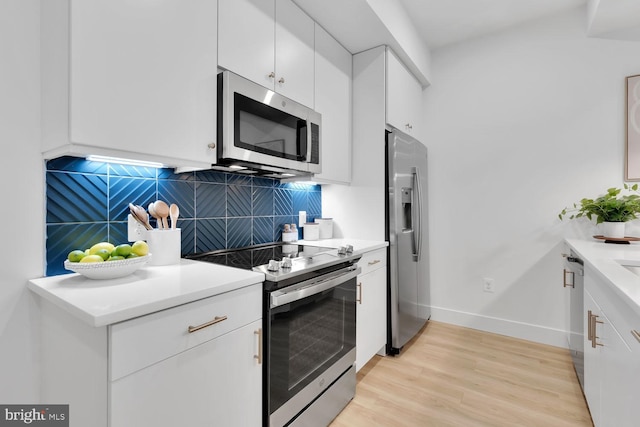 kitchen with tasteful backsplash, white cabinets, light hardwood / wood-style floors, and appliances with stainless steel finishes