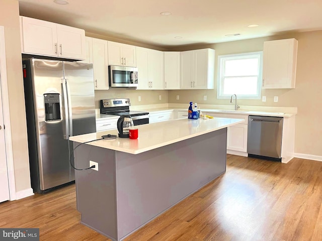 kitchen with light wood-type flooring, stainless steel appliances, a kitchen island, sink, and white cabinetry