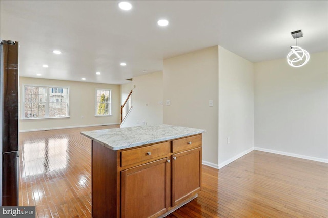 kitchen featuring light stone counters, pendant lighting, an inviting chandelier, light hardwood / wood-style flooring, and a center island